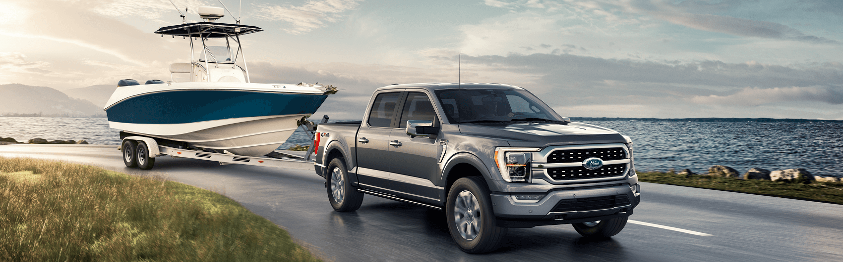 With a towing capacity of 14,000 pounds, a silver Ford F-150 easily tows a boat on a seaside road