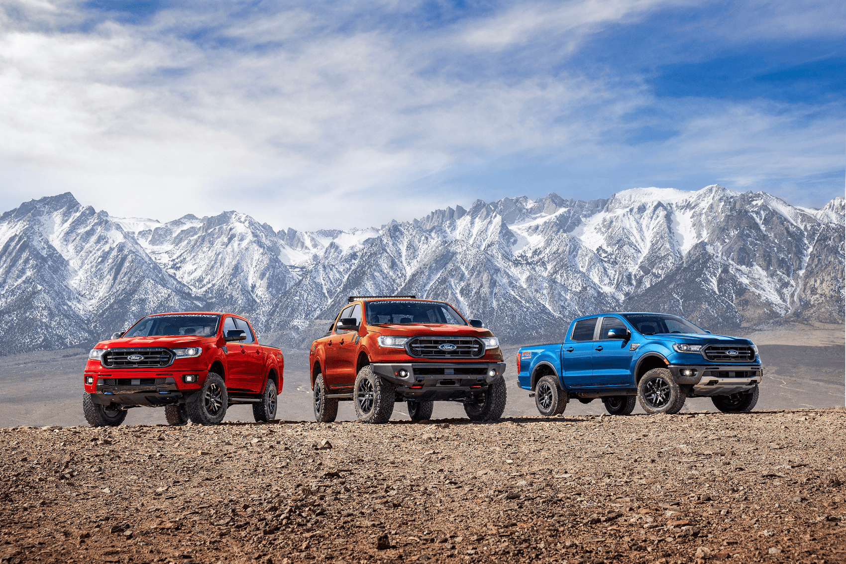 Ford Rangers in red, orange, and blue parked in front of a mountain chain